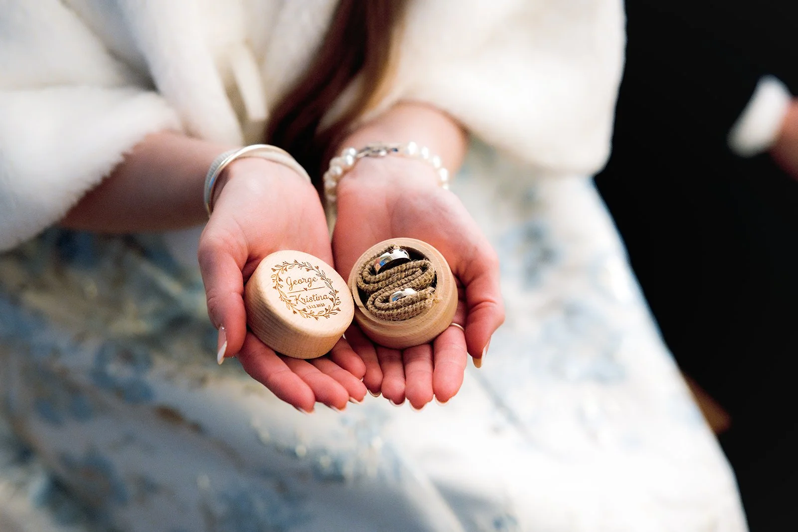 Hands holding a small wooden box with wedding rings inside, and a lid with a message engraved on it, reading 'George Kristina'. Norwich Castle wedding