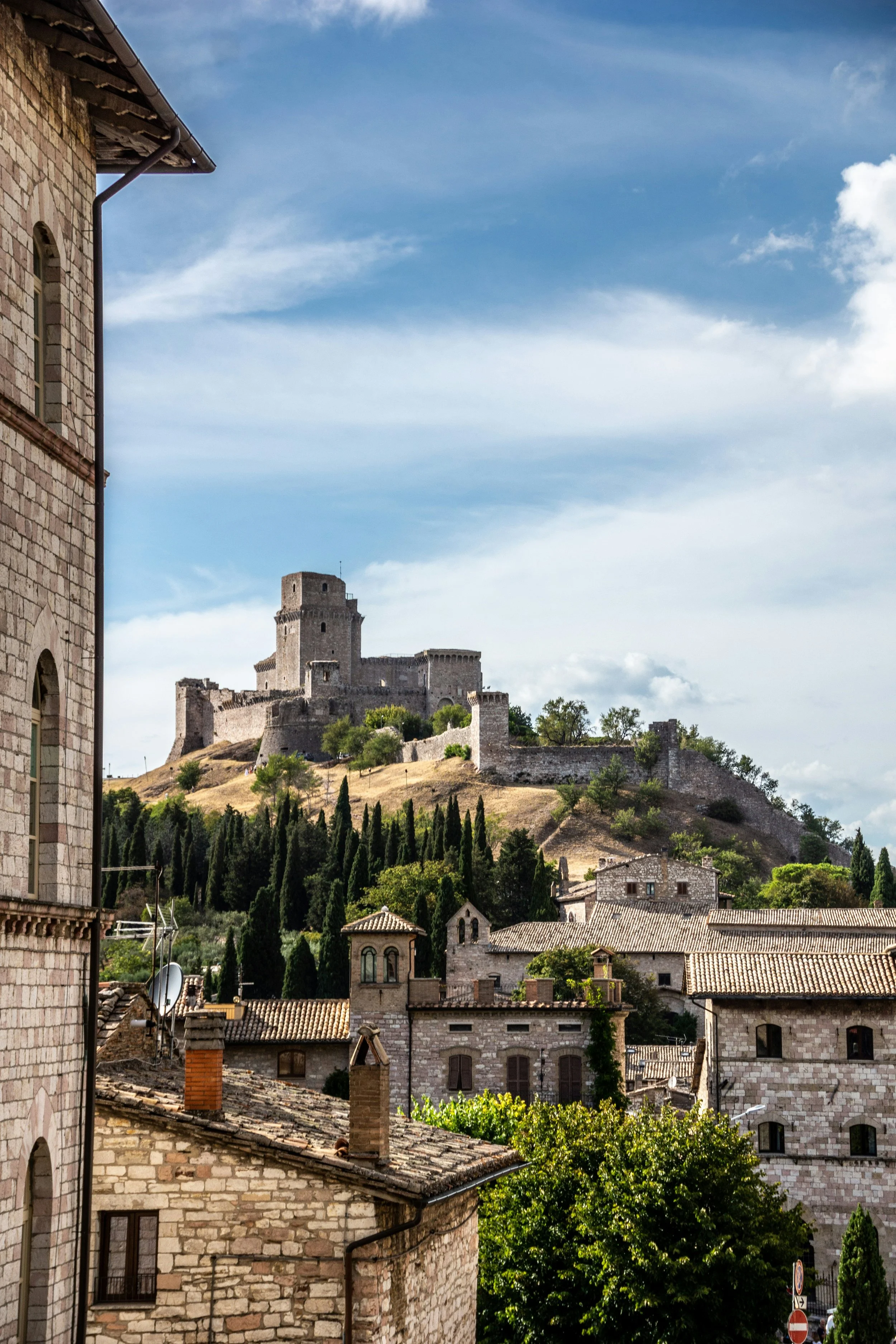 View of a historical castle situated in Umbria on a hilltop overlooking a small town with stone buildings and trees, perfect for riding and discover with bicycle.