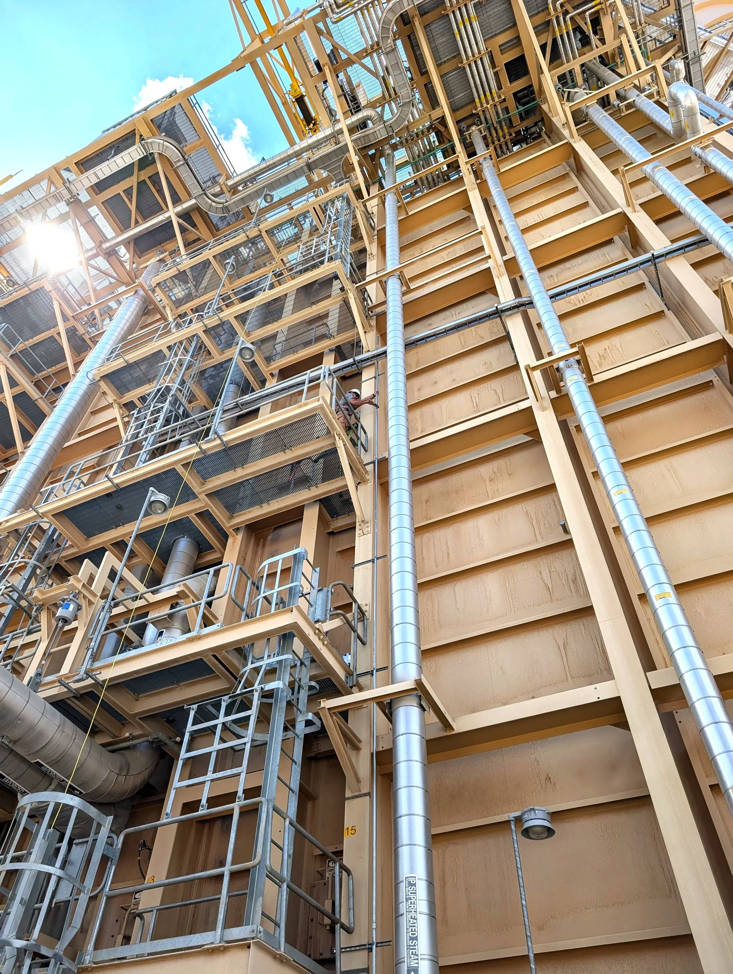 Construction site with scaffolding, large metal pipes, and wooden framework, under a blue sky with clouds.