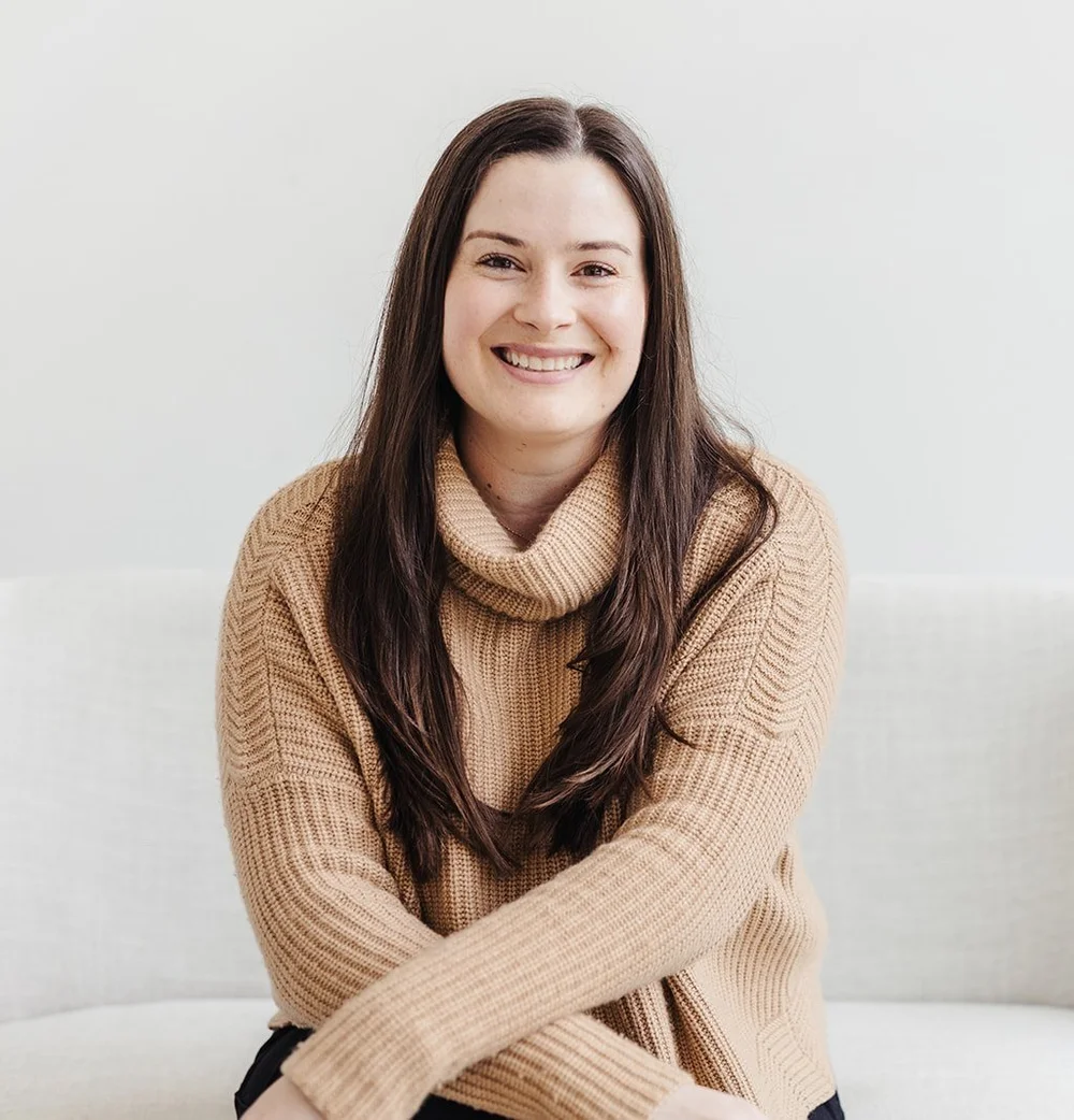 Lily Gordon, LMHC, smiling on a light couch in a tan knit sweater