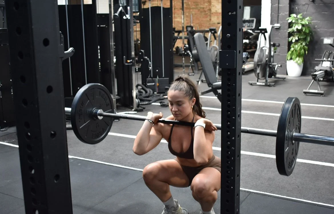A woman in workout attire squats with a barbell loaded with weights in a gym.