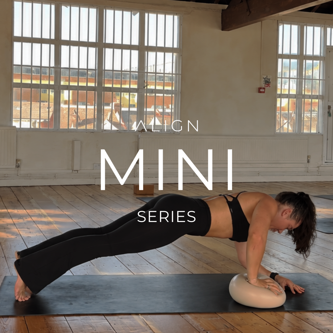 A woman practicing yoga in a sunlit room, using a yoga wheel for support while in a plank position on a black mat.