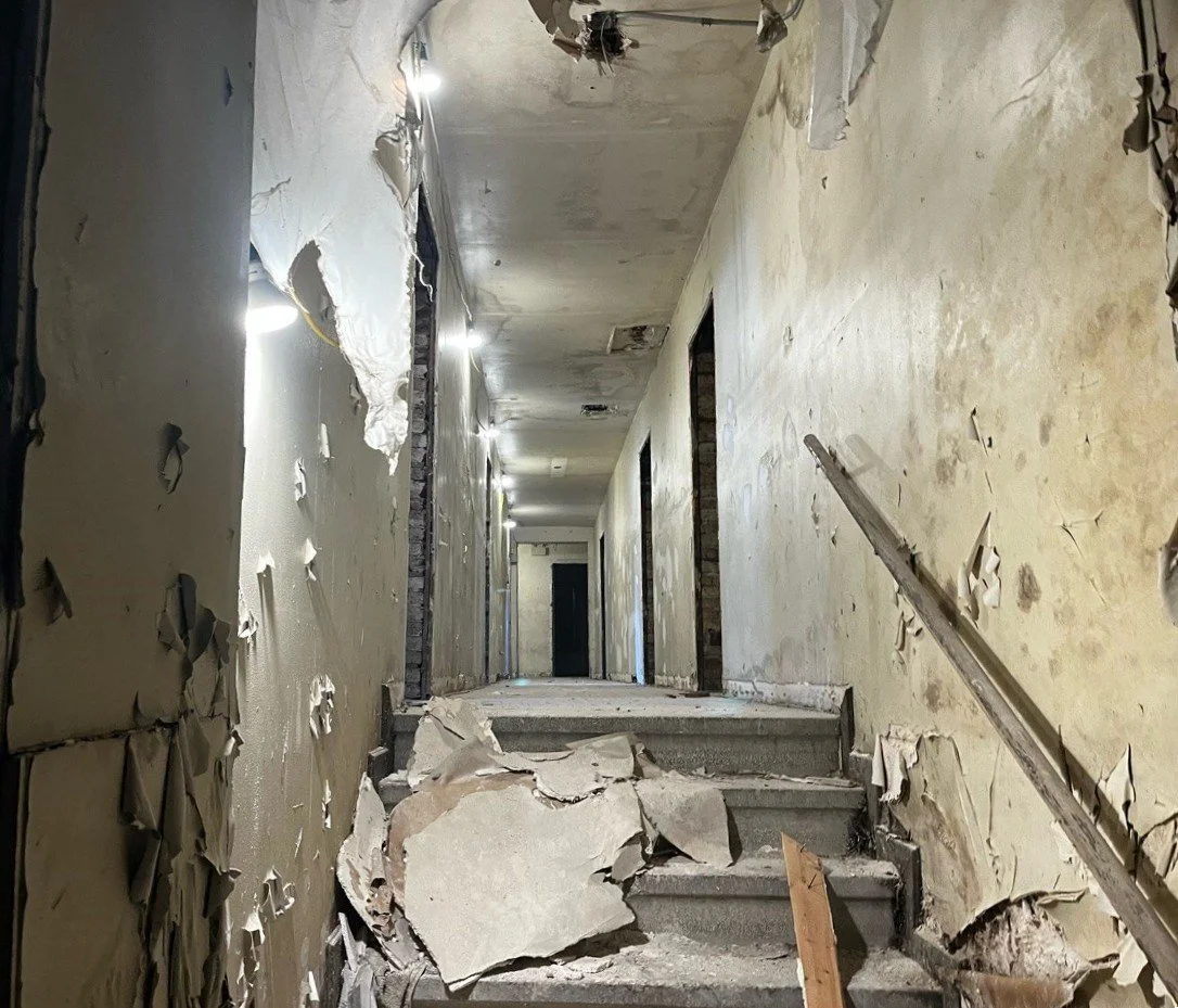 A damaged hallway with peeling paint and debris on the stairs, showing signs of destruction and disrepair.