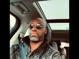 A man with long dreadlocks wearing sunglasses sitting in a car.