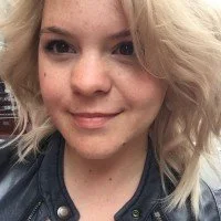 Close-up of a woman with blonde, curly hair and fair skin, smiling at the camera.