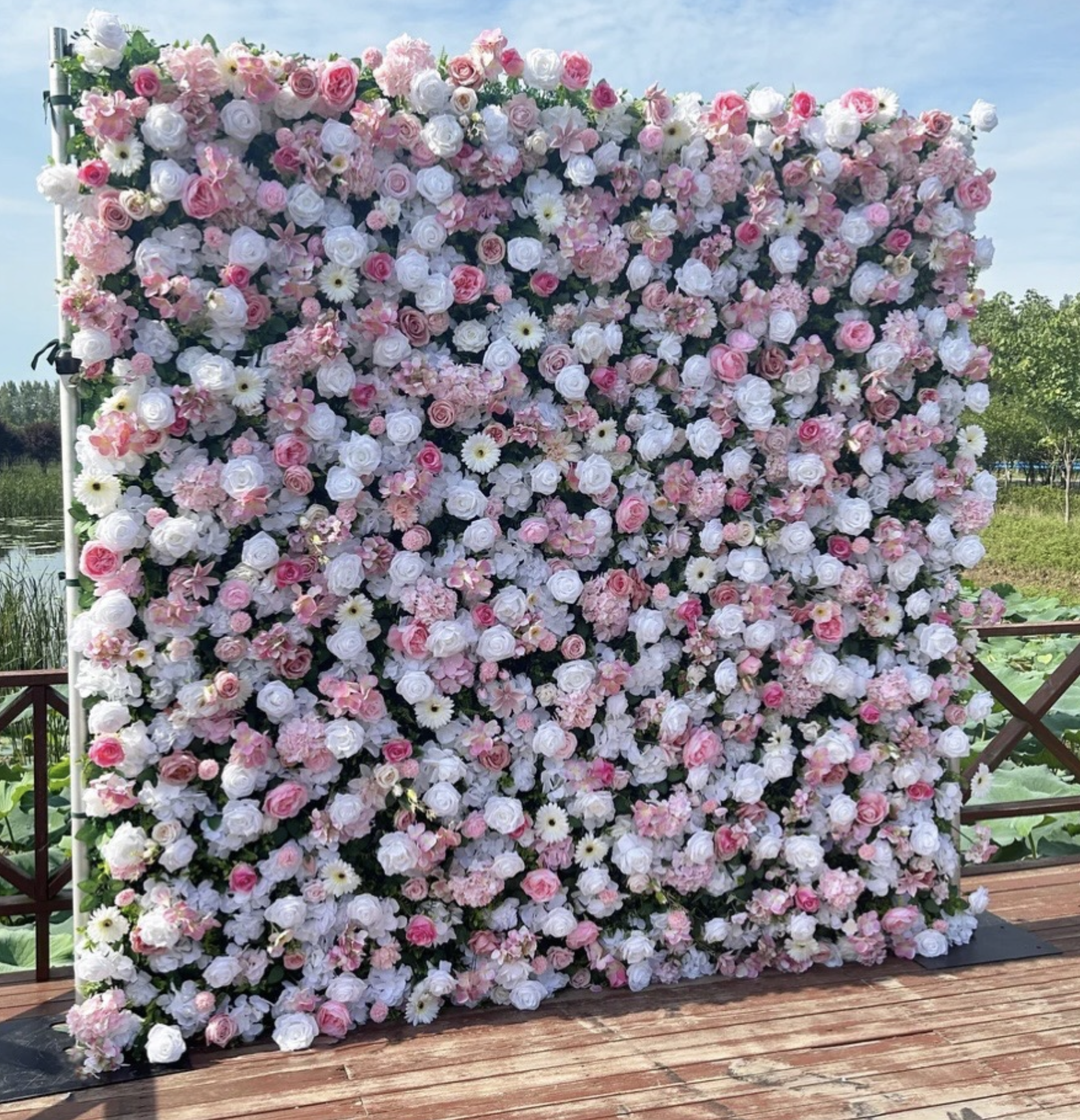 A large floral arrangement with pink and white roses, daisies, and other flowers on a wooden deck outdoors.