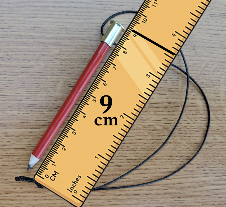 A yellow plastic ruler measuring 9 centimeters, a red pencil with a silver eraser, and a black string on a wooden surface.