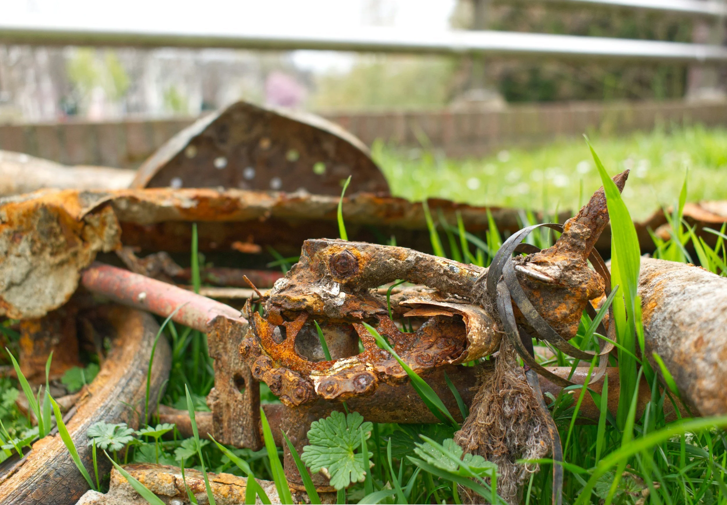 Close-up of rusted metal debris and broken pieces scattered on green grass with small plants.