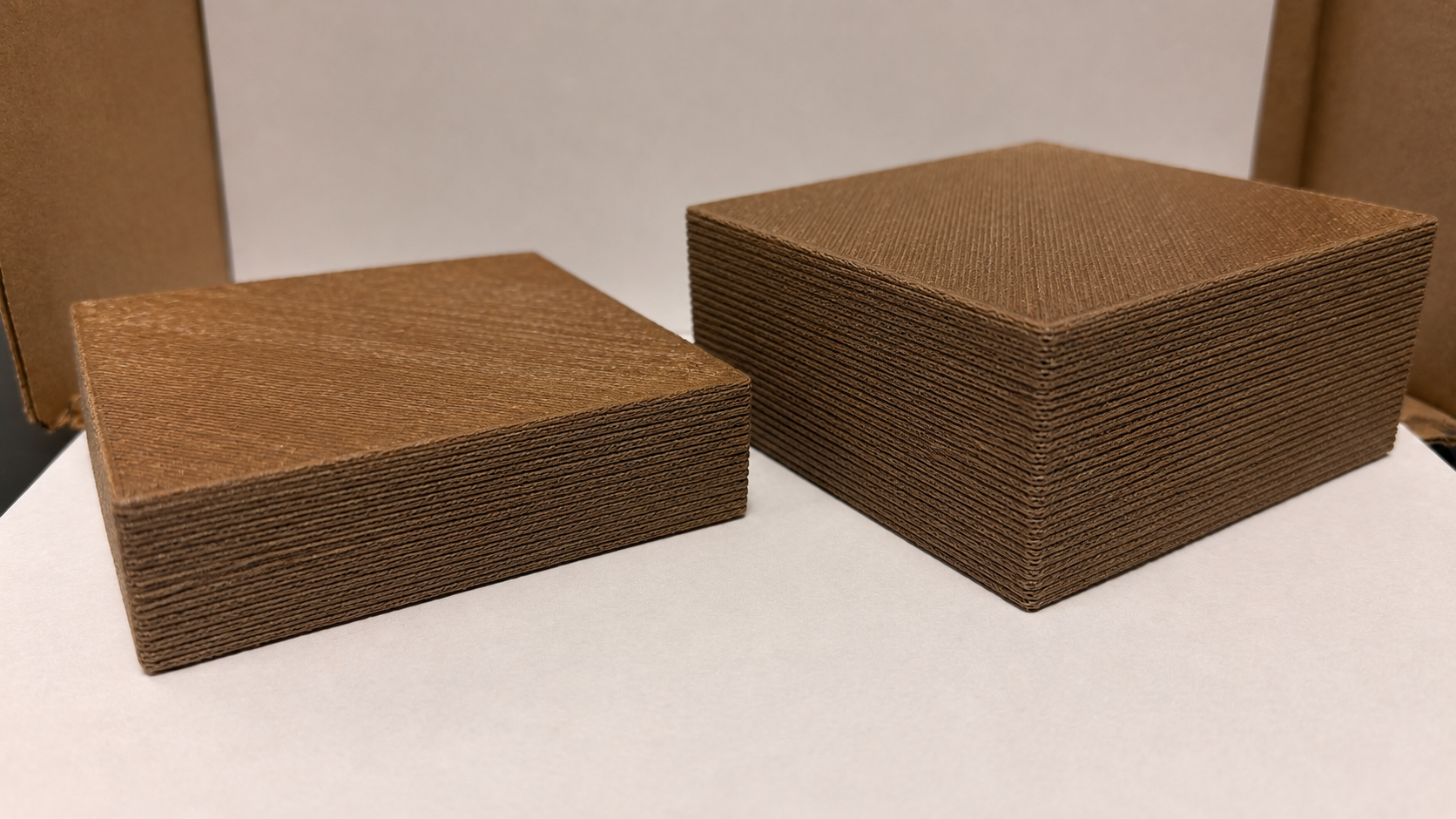 Two stacks of brown corrugated cardboard pieces placed on a white surface, with a cardboard background.