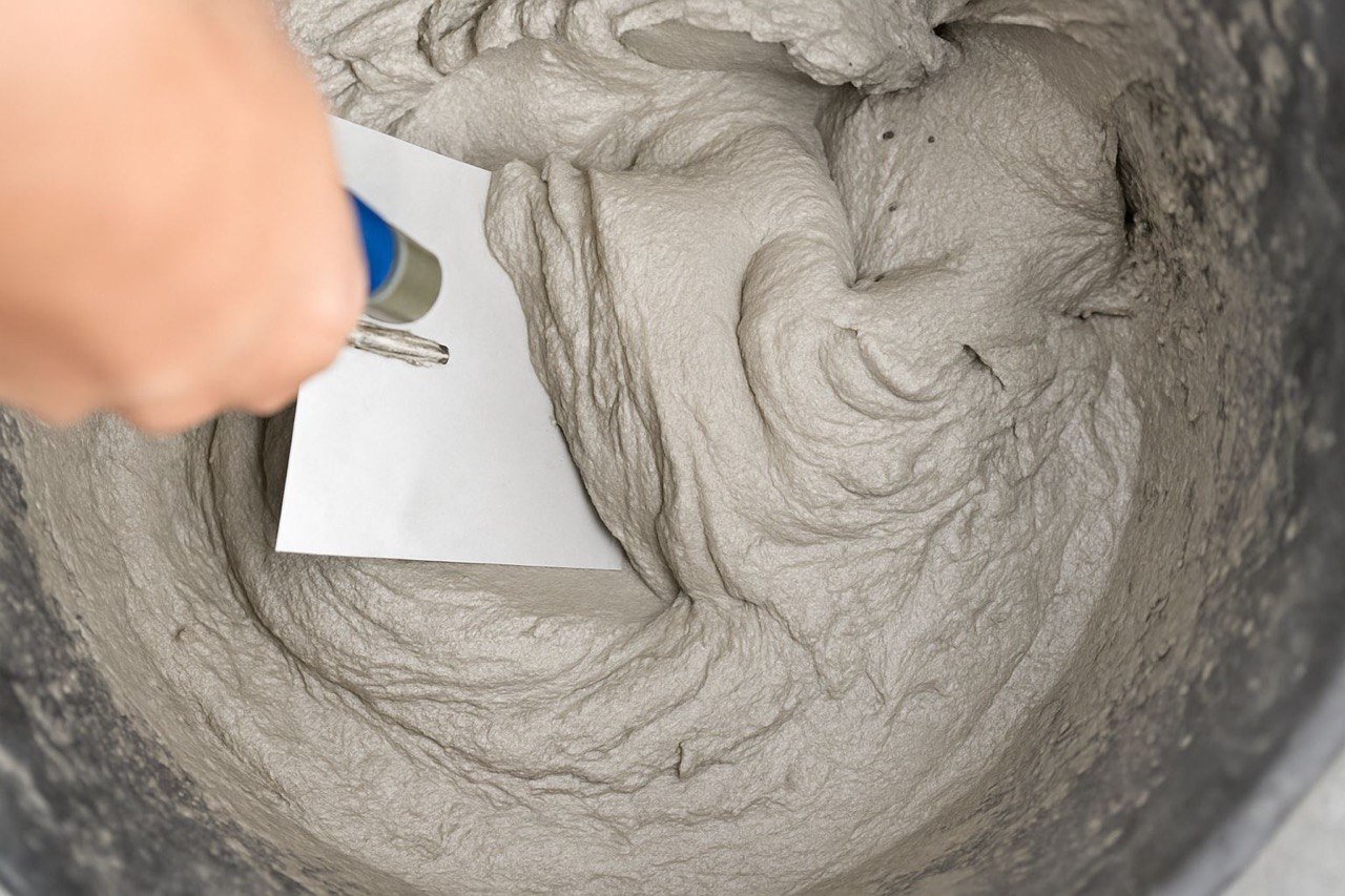 Close-up view of wet cement and a hand with a pen writing on a white piece of paper placed on the cement surface.