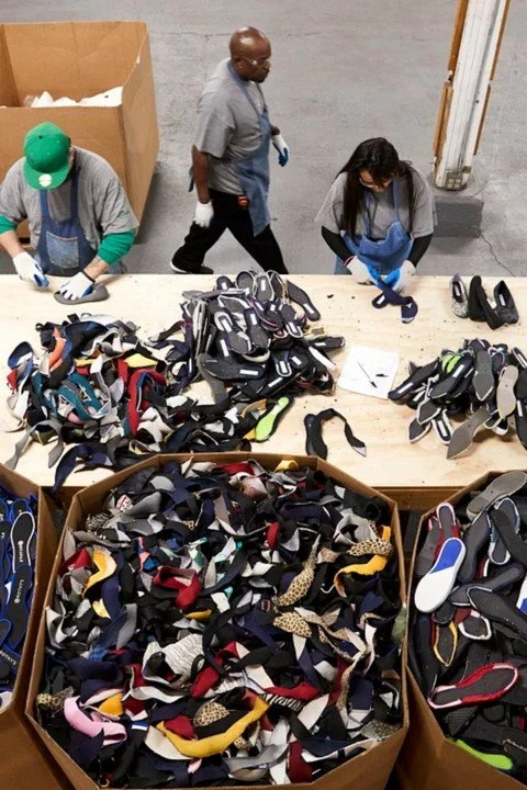 People sorting and organizing a large collection of shoes on a table in a warehouse or storage room.