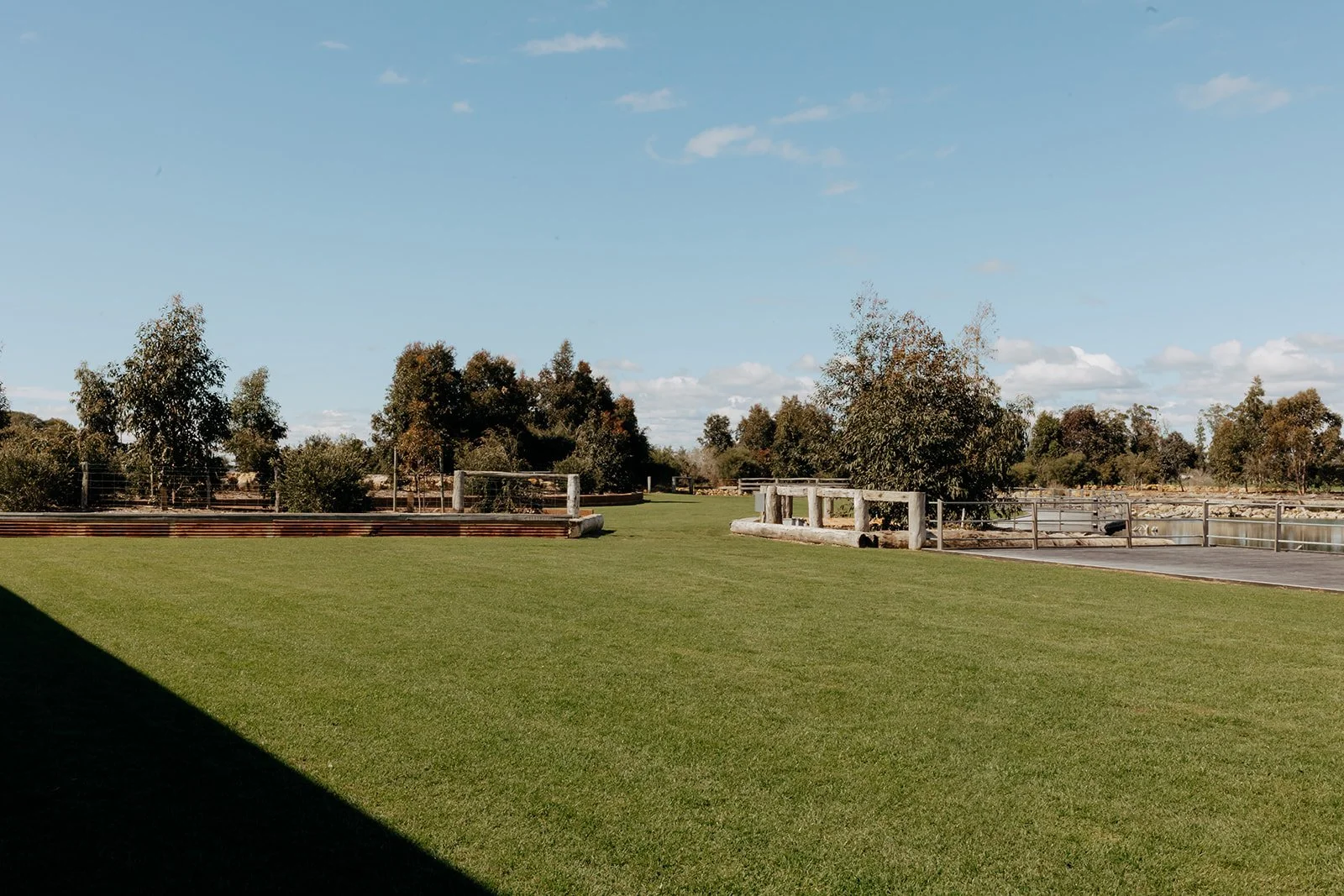 A green grassy park with trees, a fence, and a clear blue sky with a few clouds.