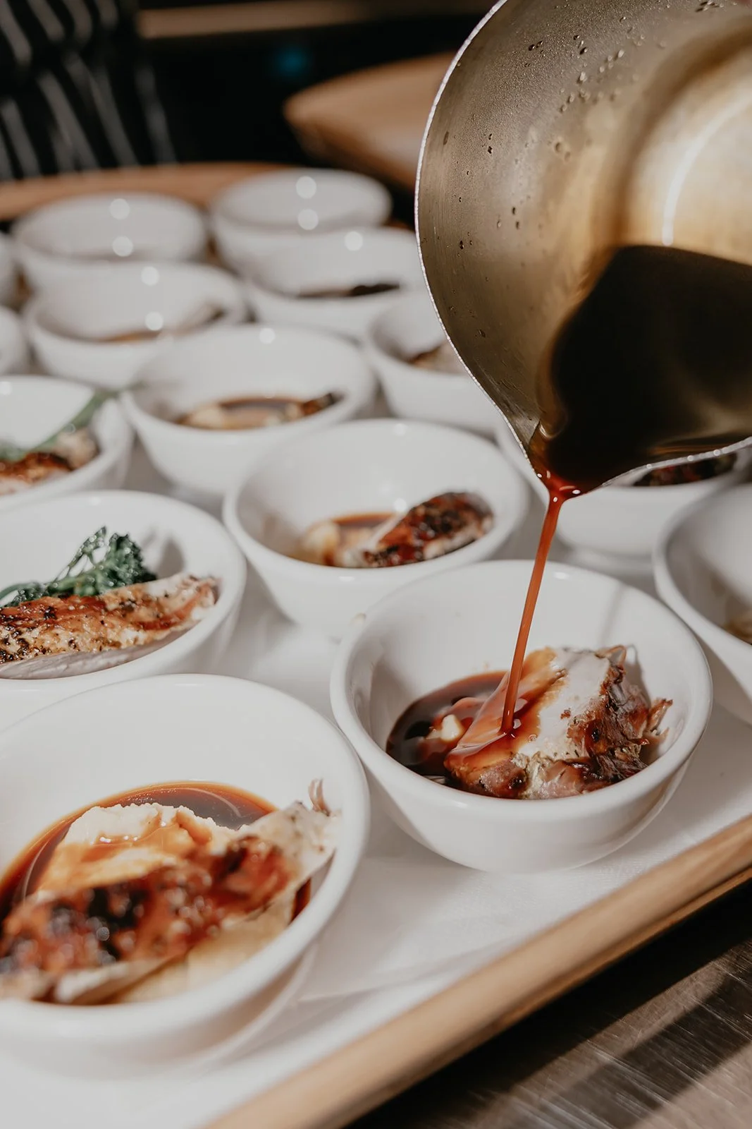 Pouring sauce over sliced roasted duck in small white bowls on a tray.