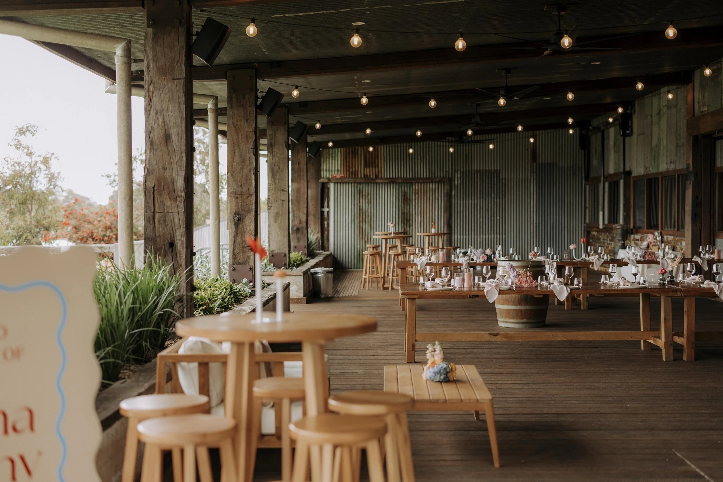 Empty rustic wedding reception area with decorated tables, string lights, and outdoor views.