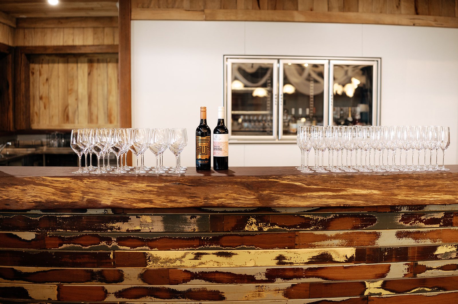 Empty wine glasses and bottles on a rustic wooden bar counter in a venue setting.