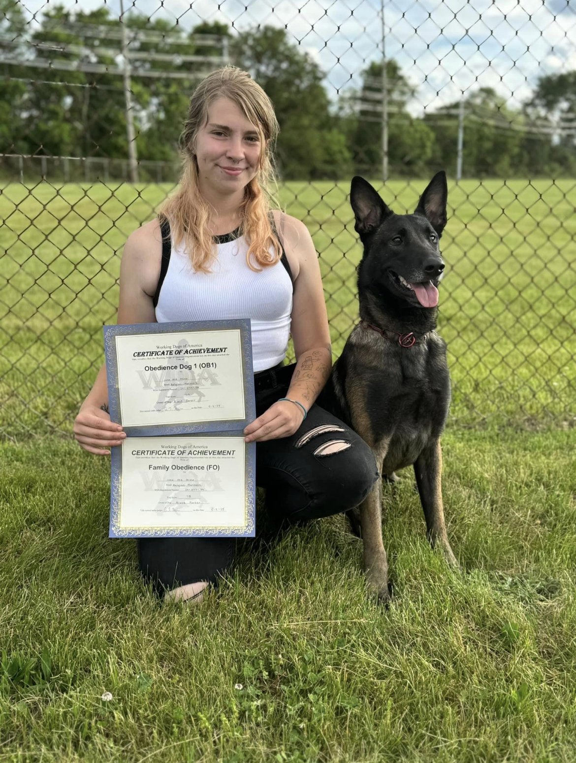 Elite dog trainer, Blaze Parker, is holding two certificates of achievement for passing a prestigious and difficult dog trial designed to test the obedience, control, skill, and bond of her Belgian Malinois. the team earned the FO and OB1 title.