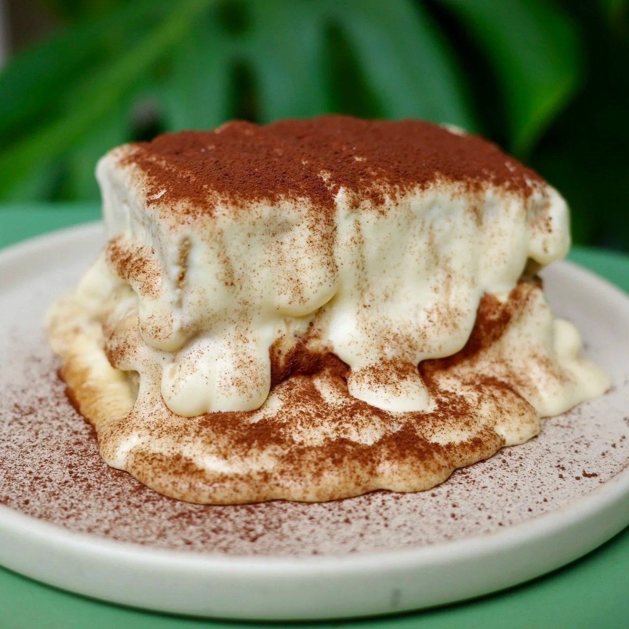 A serving of tiramisu dessert topped with cocoa powder on a white plate.