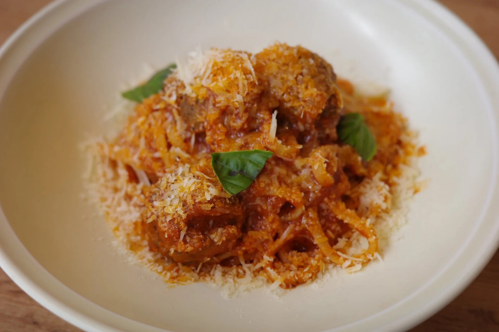 Bowl of spaghetti with meatballs, shredded cheese, and basil leaves.