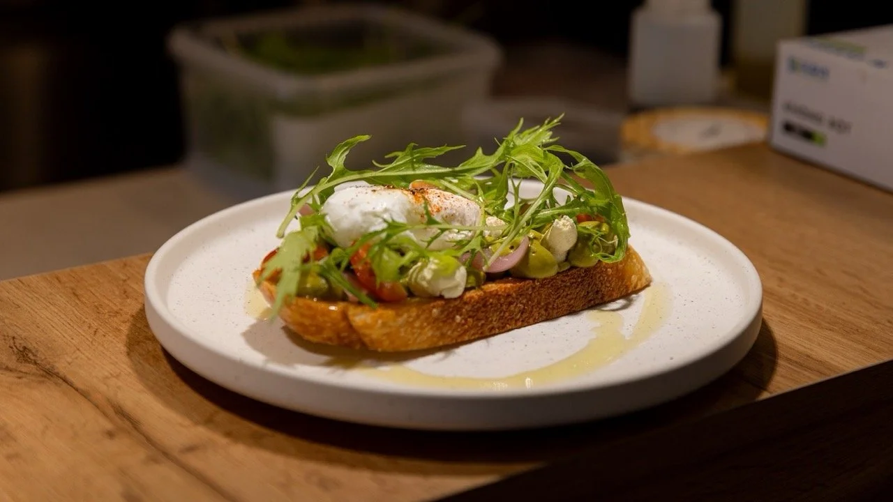 Open-faced sandwich with green salad, dollops of cheese, and a poached egg on toasted bread, drizzled with olive oil