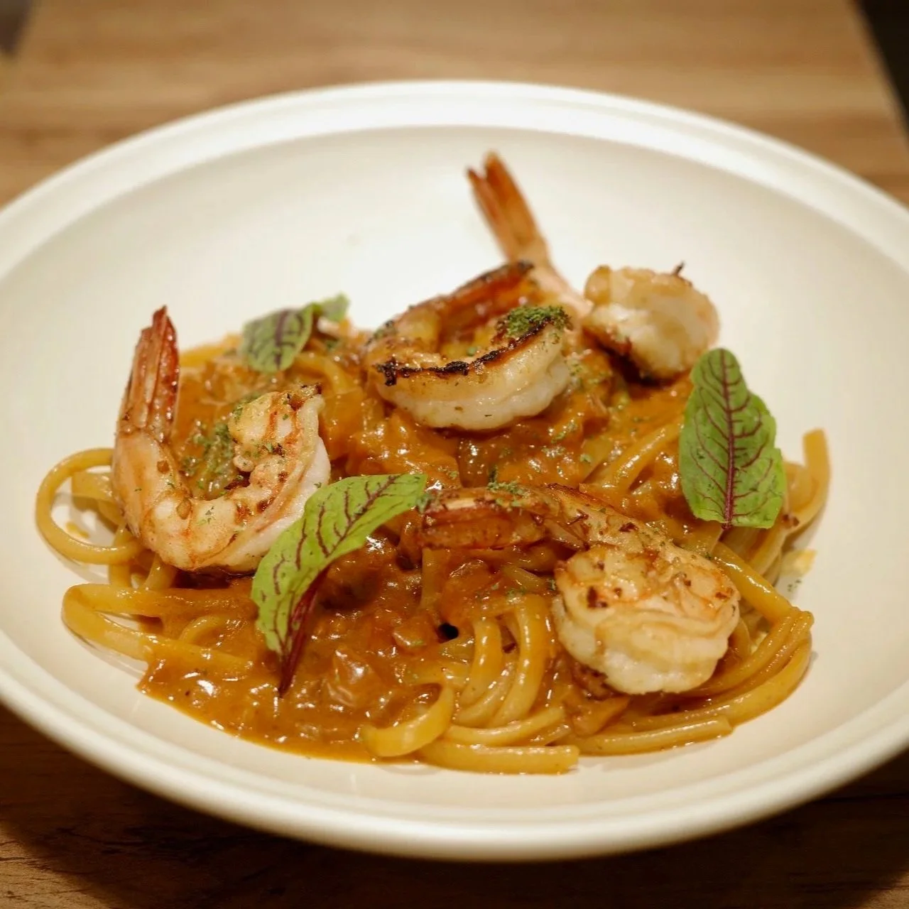 A plate of spaghetti topped with shrimp, a tomato-based sauce, and garnished with small green leaves.