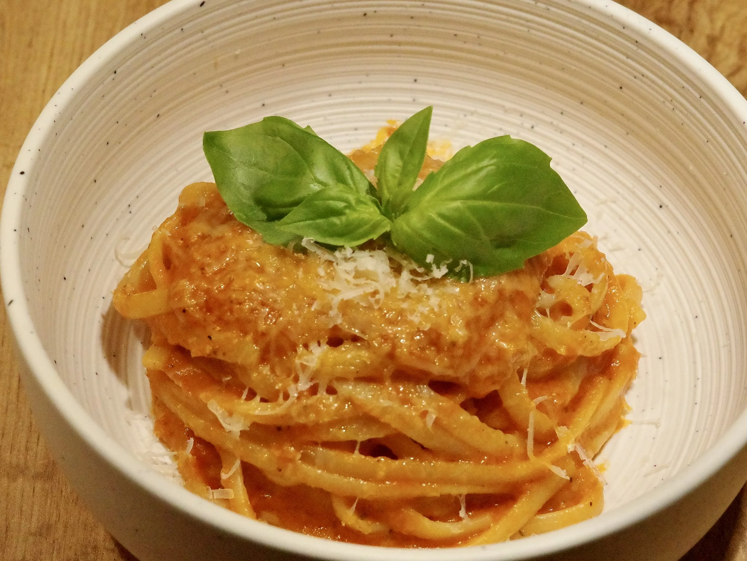 A bowl of fettuccine pasta with tomato sauce, topped with shredded cheese and fresh basil leaves.