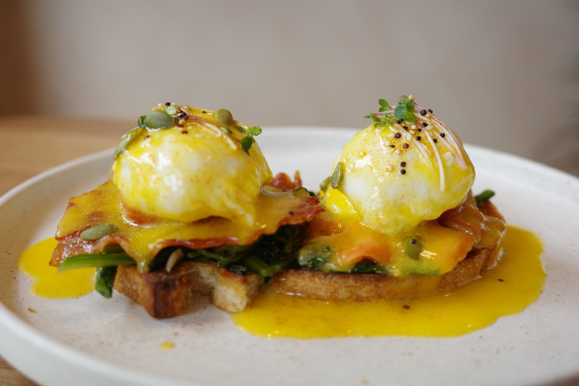 Close-up of eggs Benedict with hollandaise sauce, garnished with microgreens and pepper, served on toasted bread with a bed of fried vegetables.