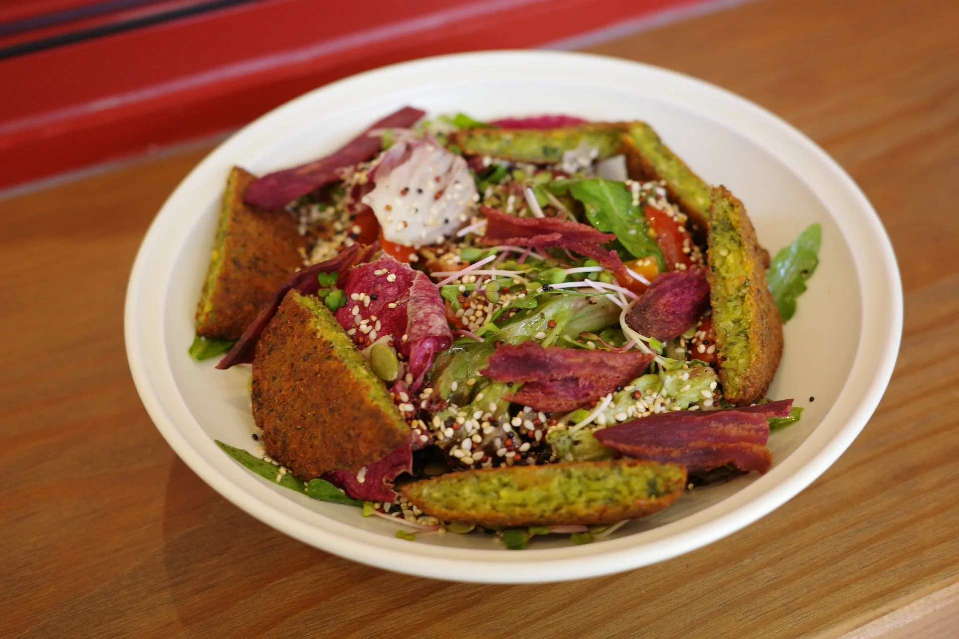Vegan salad in a white bowl with mixed greens, sliced beets, diced tomatoes, inside a seasoned edible bowl on a wooden table.
