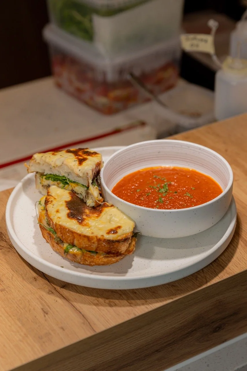 Grilled cheese sandwich with tomato soup garnished with herbs on a white plate.