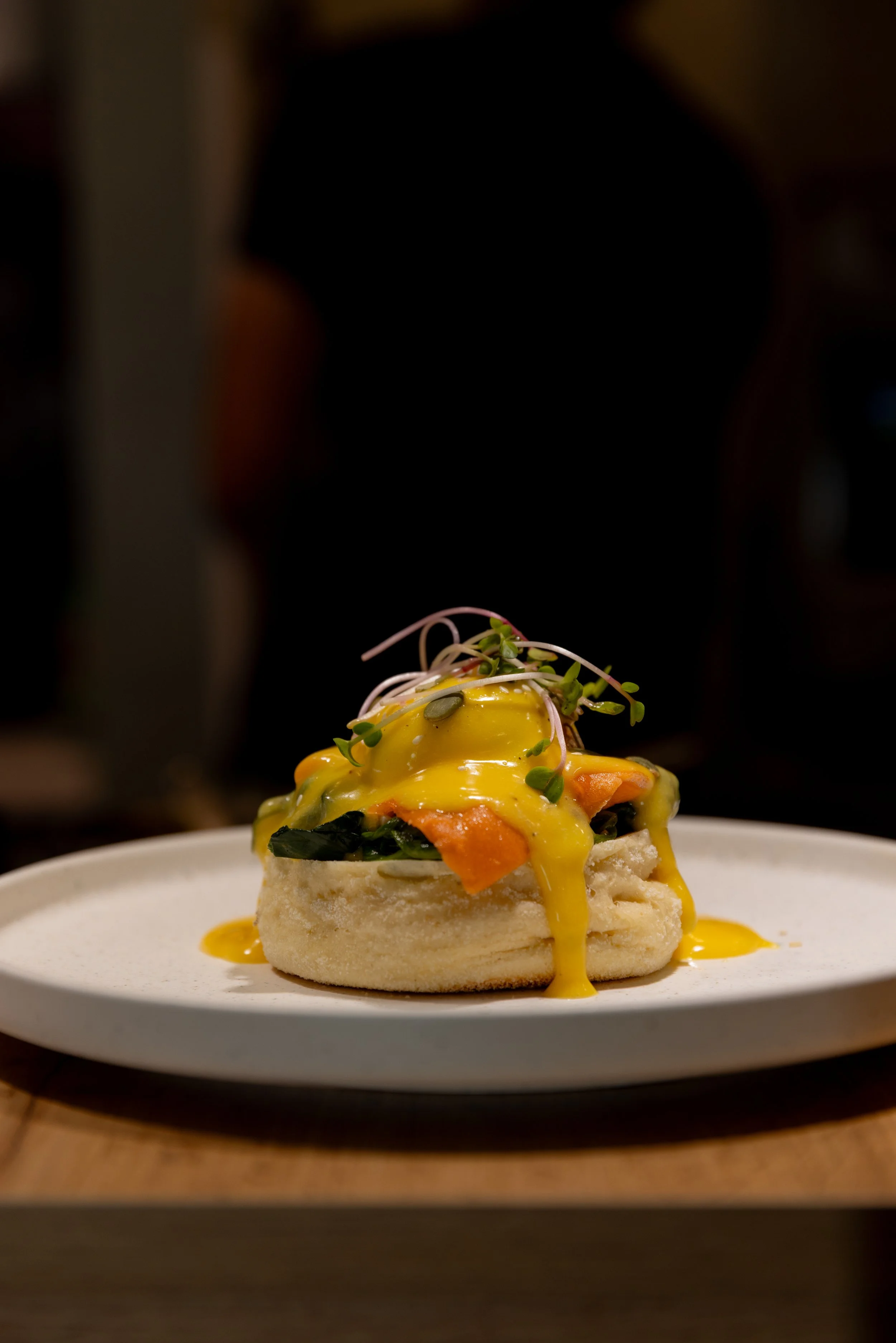 Aplate of eggs benedict with hollandaise sauce, greens, and microgreens on a white plate