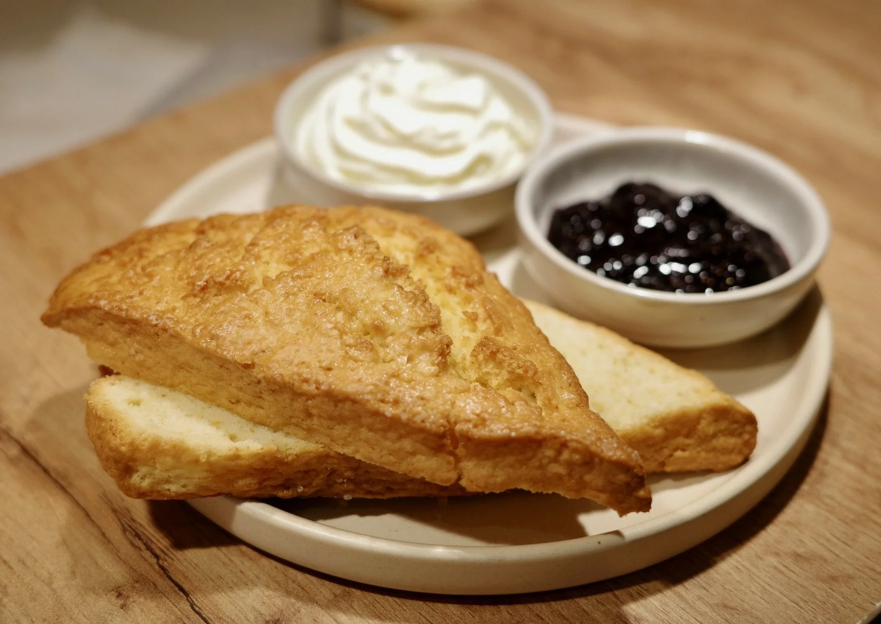 A plate of French toast with whipped cream, blueberry jam, and butter served on a round white dish on a wooden table.