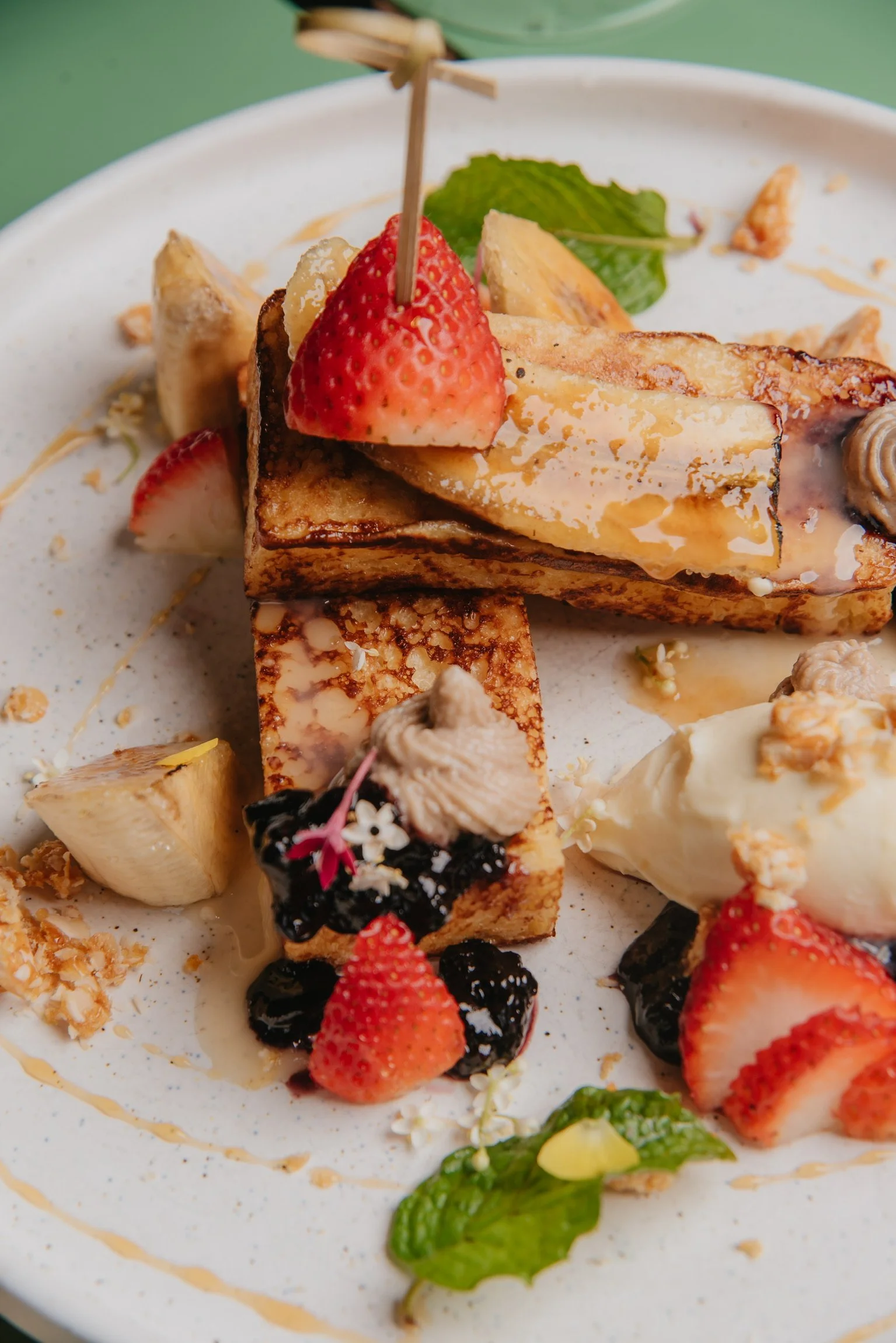 Assorted dessert plate with strawberries, bananas, edible flowers, microgreens, and syrup drizzle.