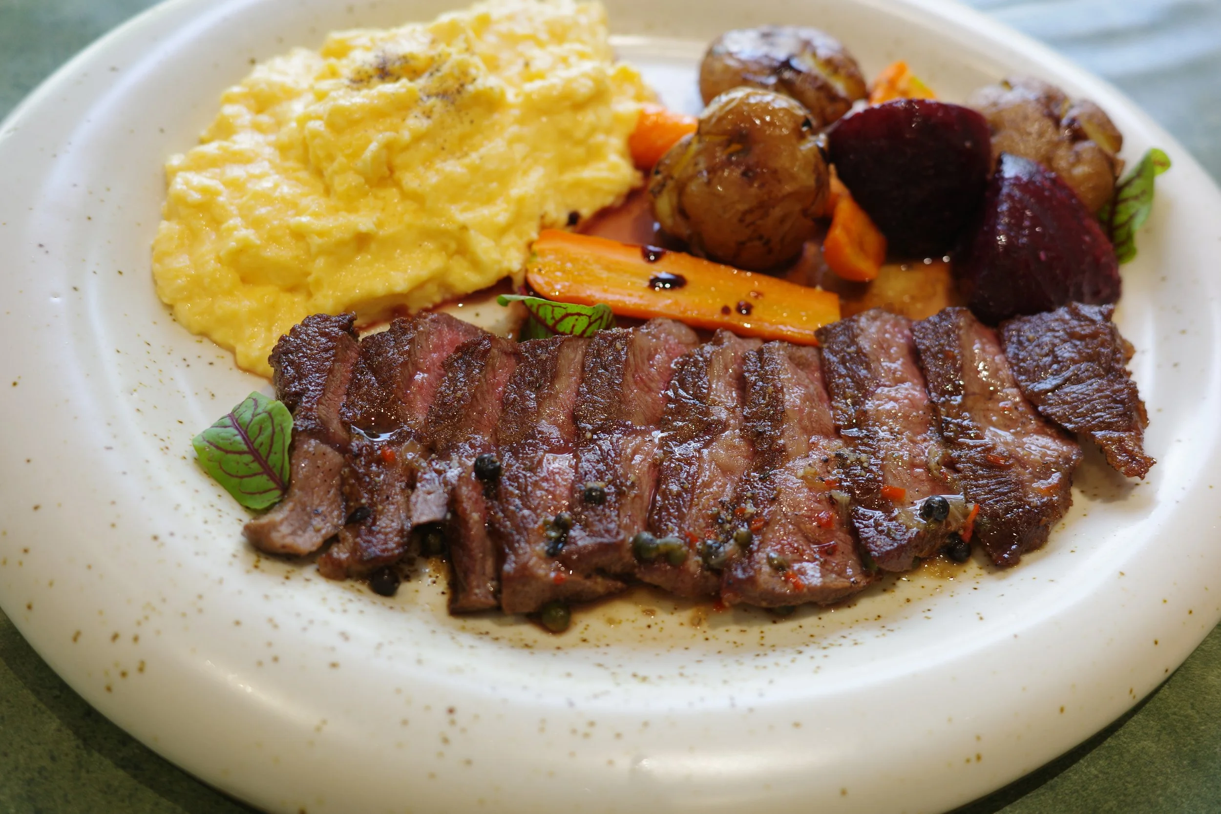 A plate of food with scrambled eggs, roasted vegetables, and sliced steak garnished with small green herbs.