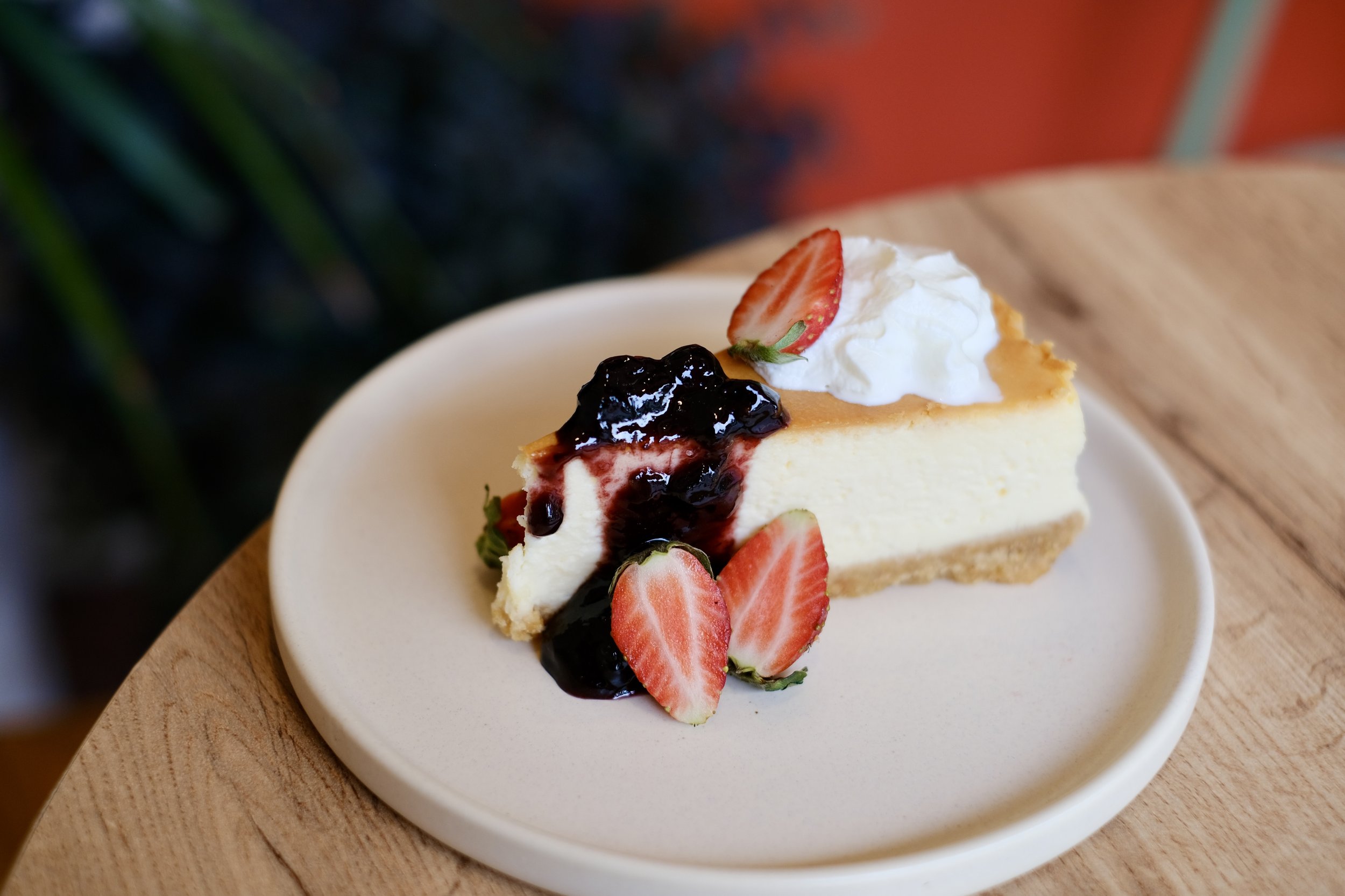 Slice of cheesecake with whipped cream, strawberry slices, and blueberry topping on a white plate