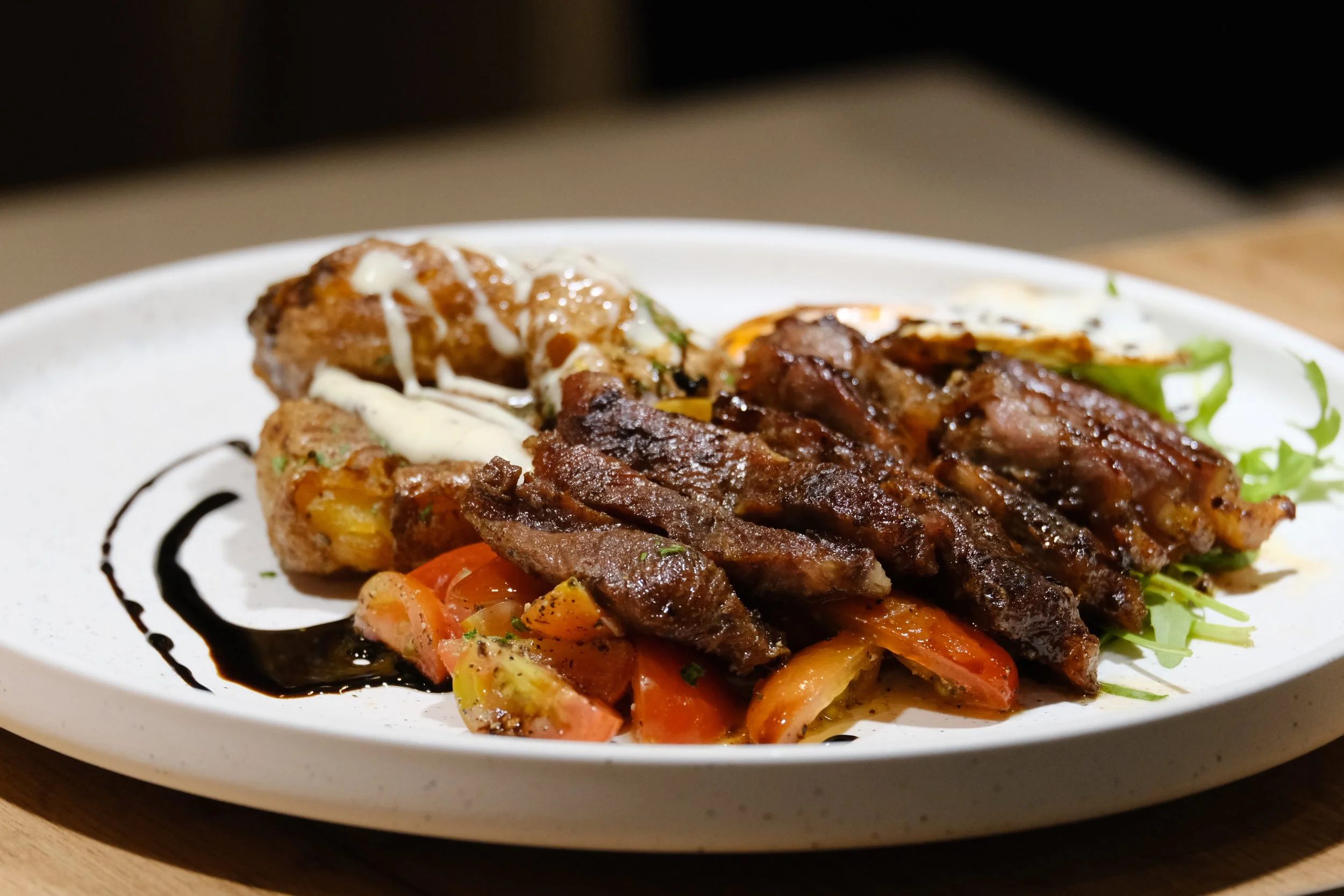 Plate of grilled steak, roasted vegetables, and two roasted potatoes with white sauce, garnished with greens, on a white ceramic plate.
