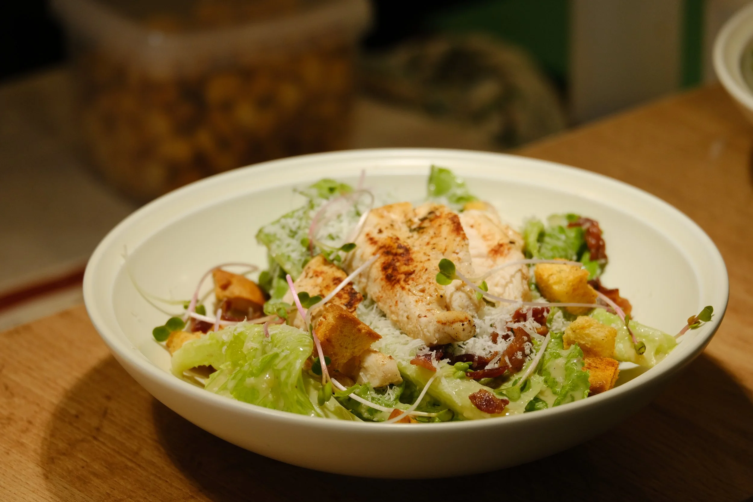 Bowl of salad with grilled chicken, lettuce, croutons, shredded cheese, and microgreens.