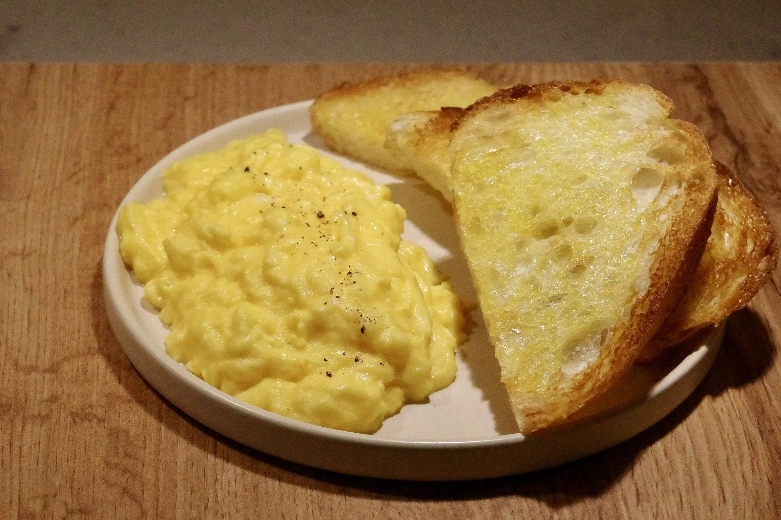 Scrambled eggs with black pepper served with two slices of toasted bread on a white plate.