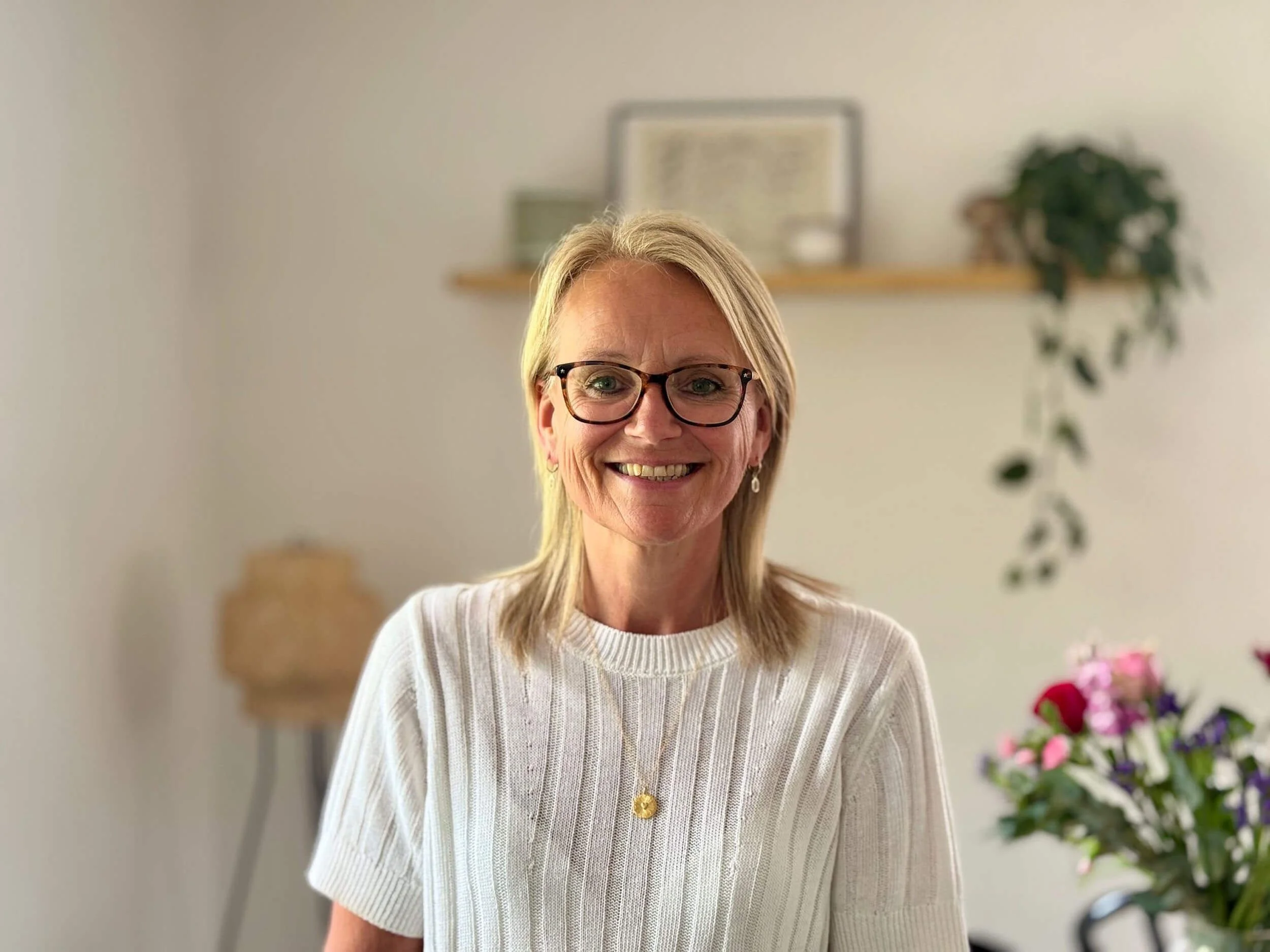 Sally Blackmore counsellor standing in a room with plants and a shelf in the background.
