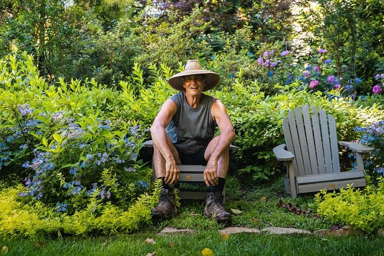 image of Chuck Hutchison with a straw hat sitting on a chair in his garden.