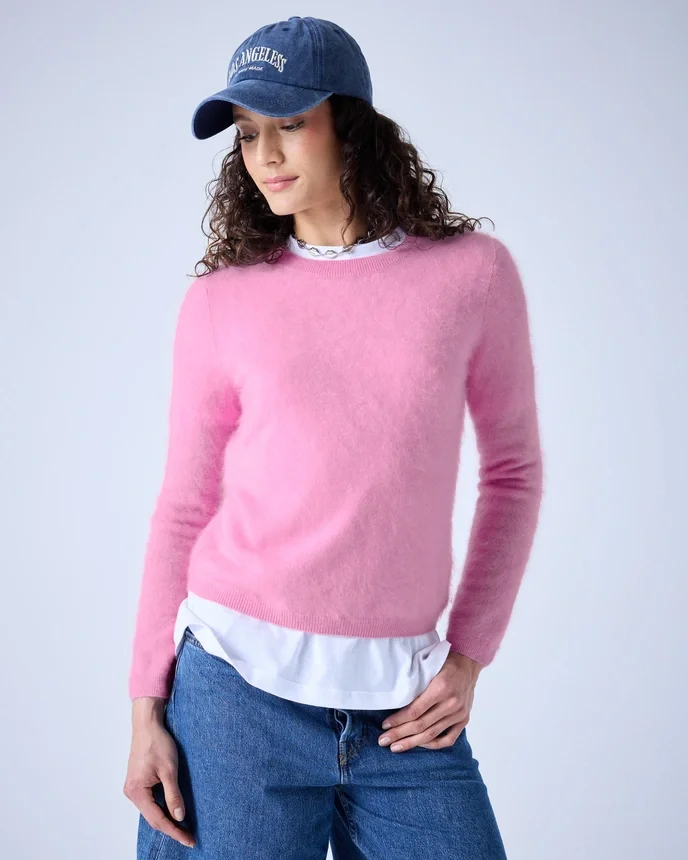 Frau trägt pinken Pullover, weiße Hemdbluse, blauen Jeans und blaue Kappe mit weißer Aufschrift.