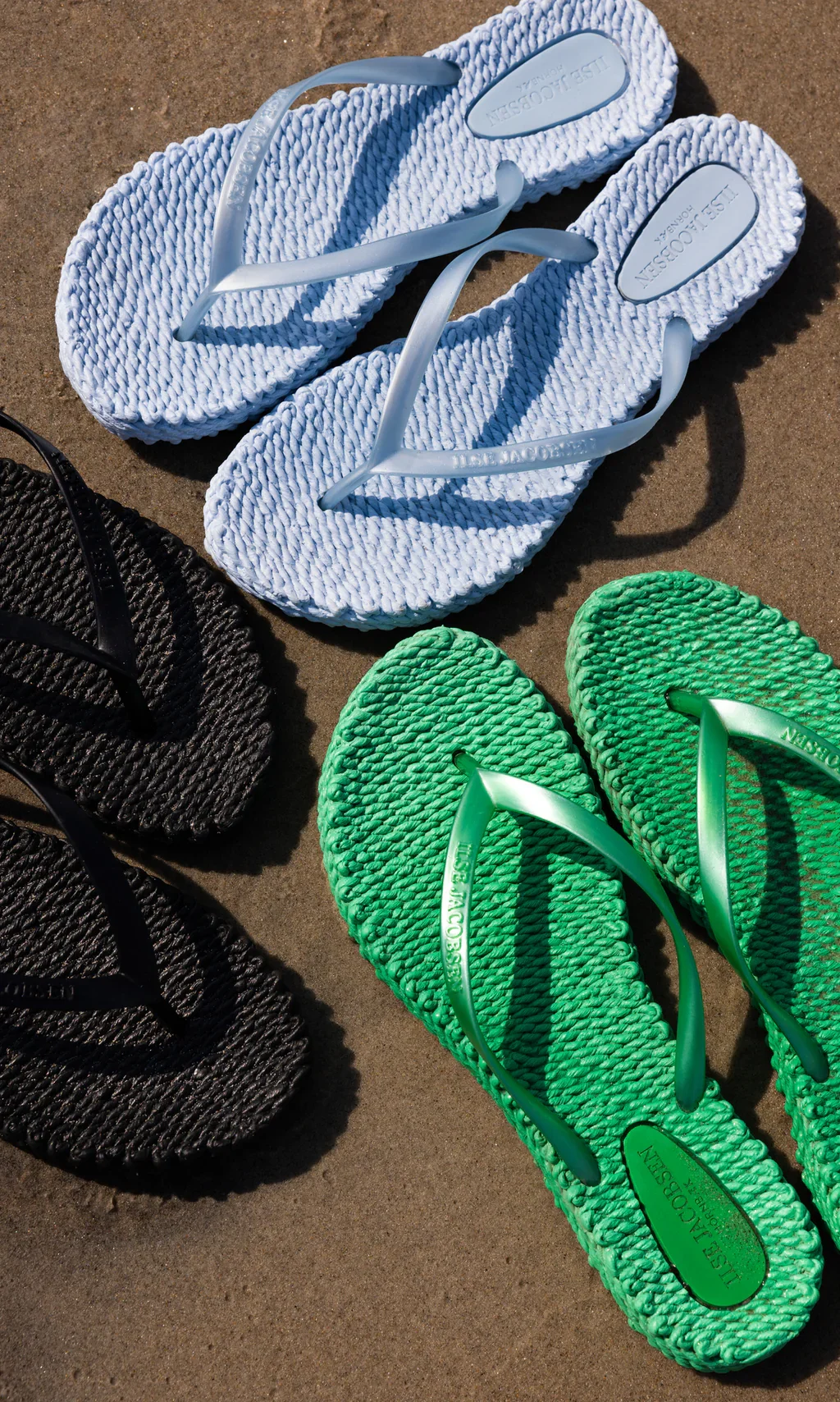 Bunte Sandalen in Weiß, Schwarz und Grün liegen auf dem Sand.