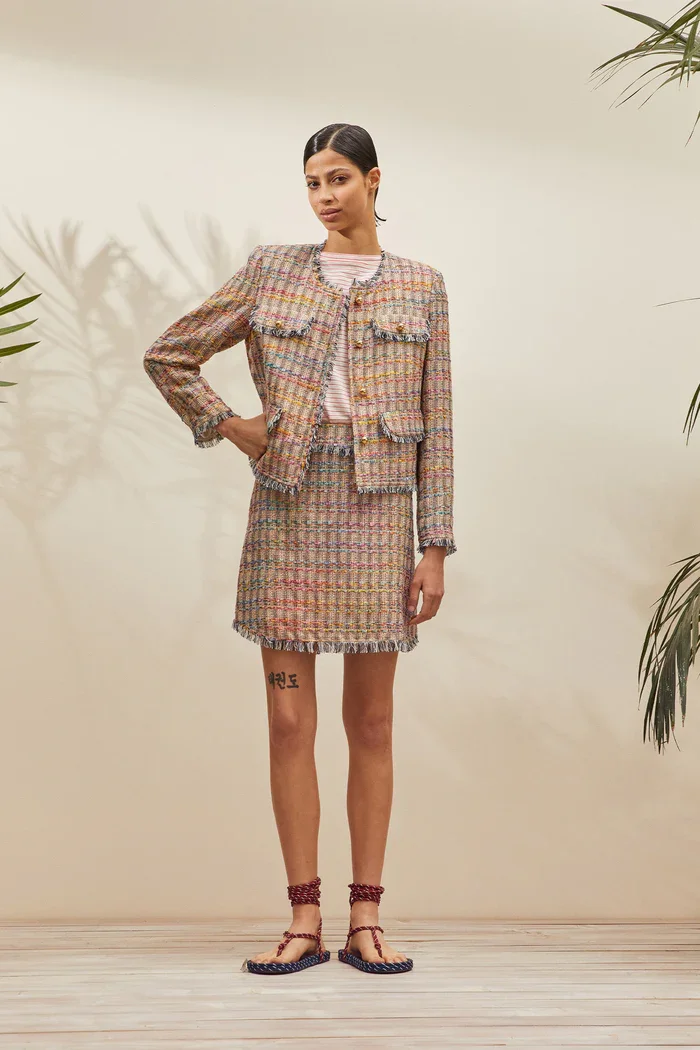 Eine Frau trägt einen Tweed-Kostüm aus Jacke und Rock, dazu Sandalen mit Riemen.