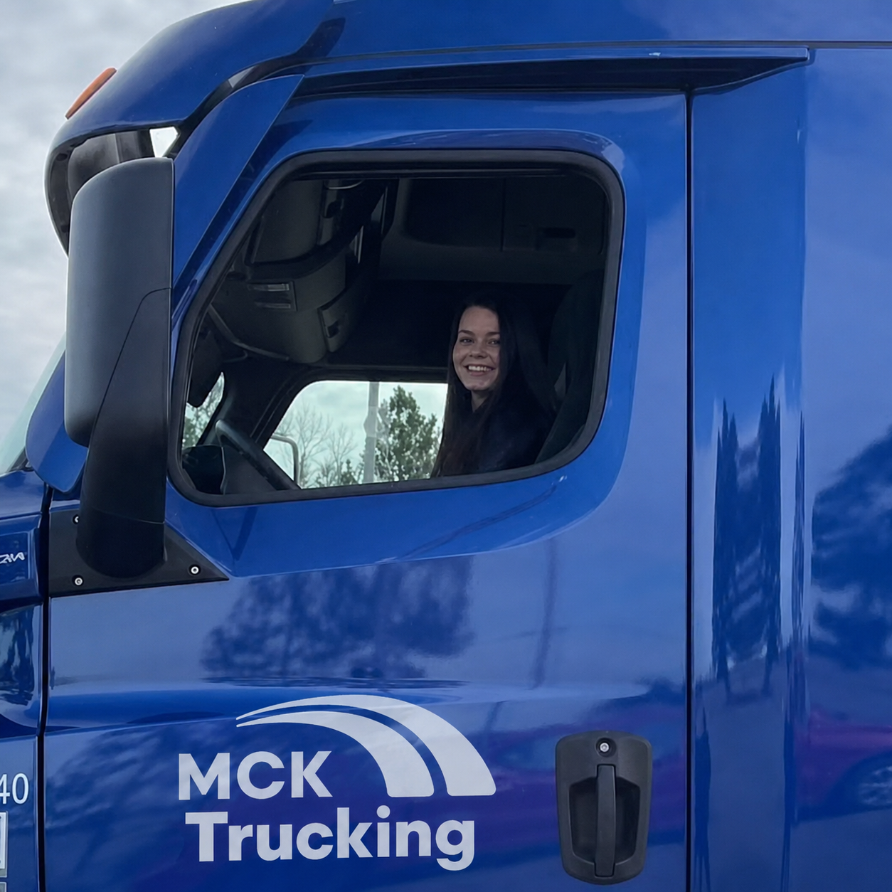 Woman smiling inside a blue truck with 'MCK Trucking' logo on the door.