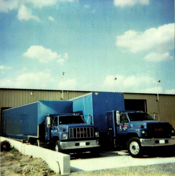Image of 2 trucks circa 1990s parked in front of a warehouse