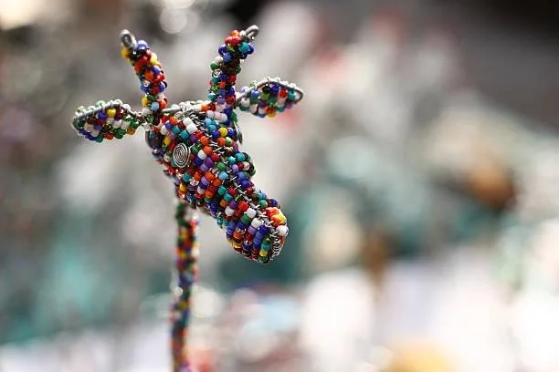 Colorful beaded sculpture resembling a rabbit with long ears, mounted on a stick, in a blurred outdoor setting.