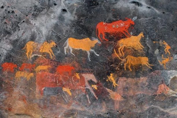 Ancient cave wall painting depicting a herd of bison in red, orange, and yellow colors.
