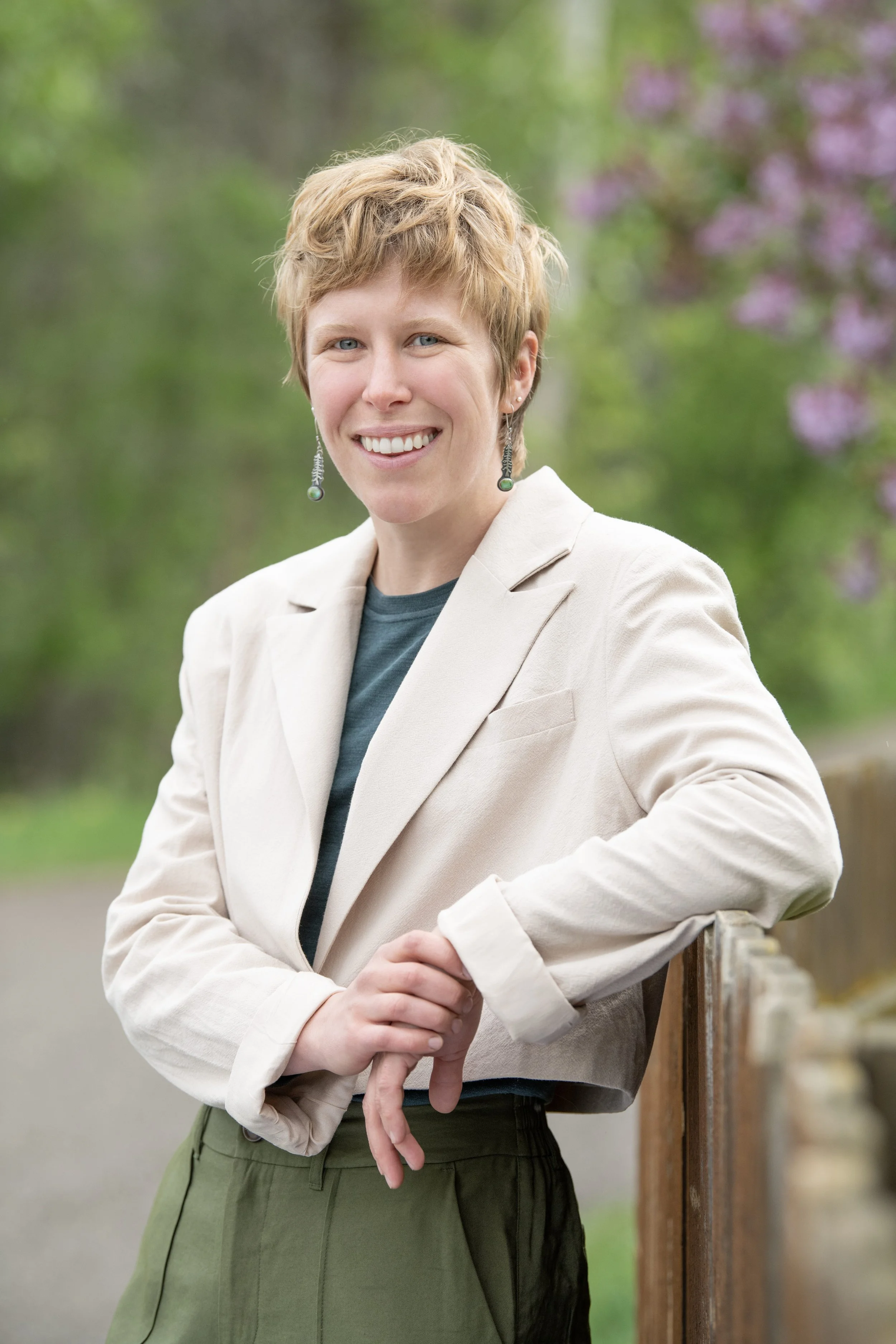 Emma Bode wearing cropped, natural cream color blazer, blue top, and olive pants smiling, looking toward camera