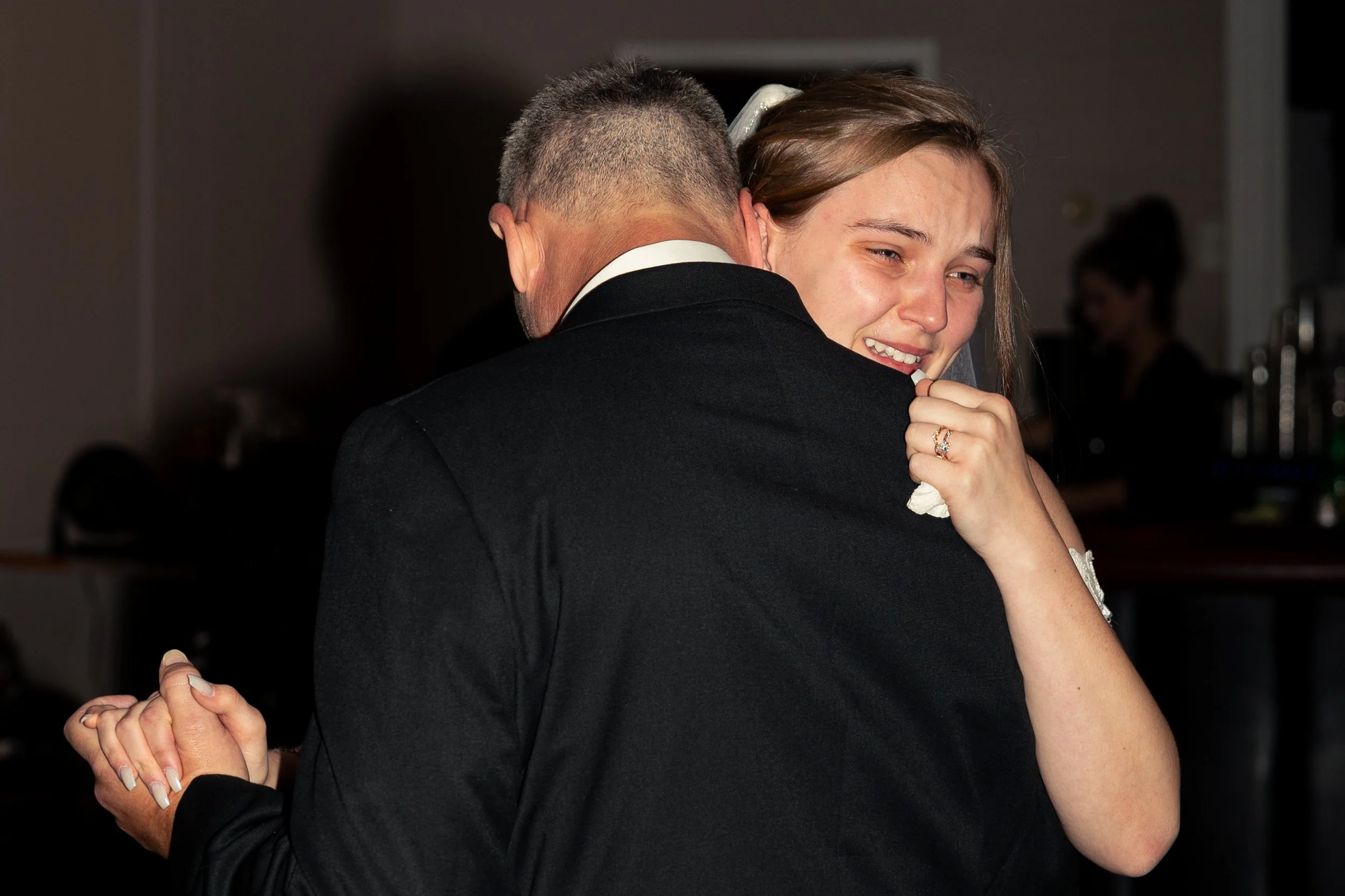A young woman is crying and clinging to an older man as they dance together at a formal event.