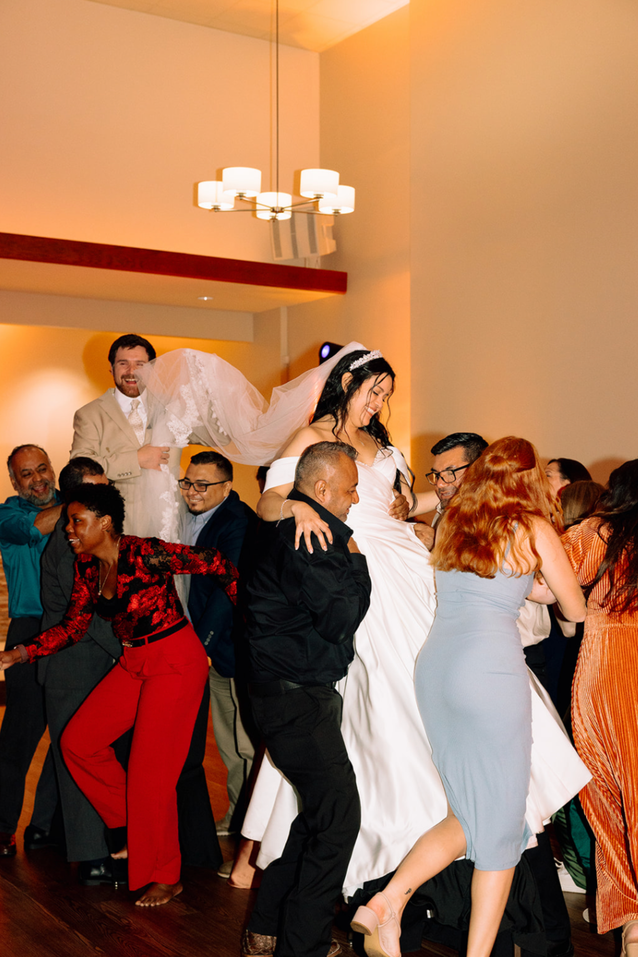 Group of people celebrating at a wedding reception, with the bride lifted above their heads.
