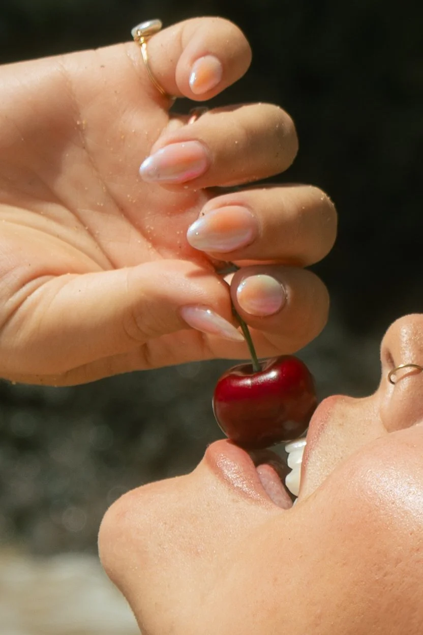 Close-up of a hand holding a cherry above a person's open mouth, which is ready to take a bite.
