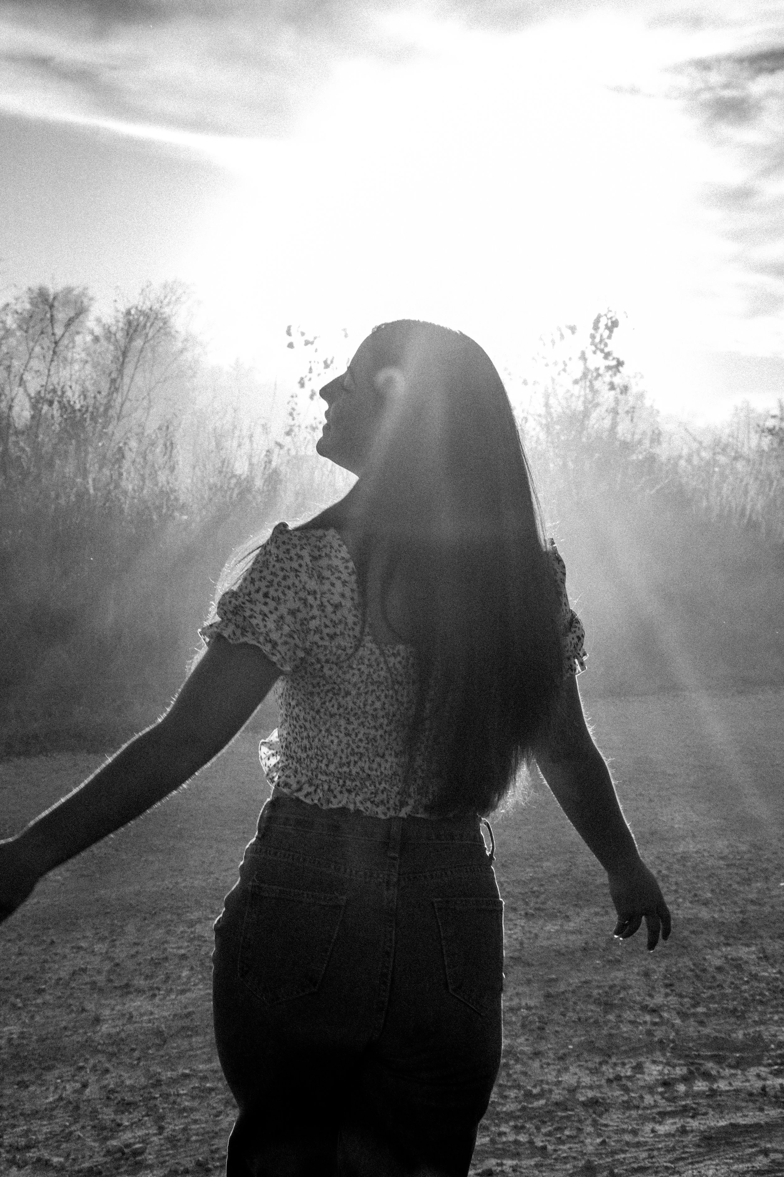 Silhouette of a woman outdoors in sunlight, facing left, with trees in the background.
